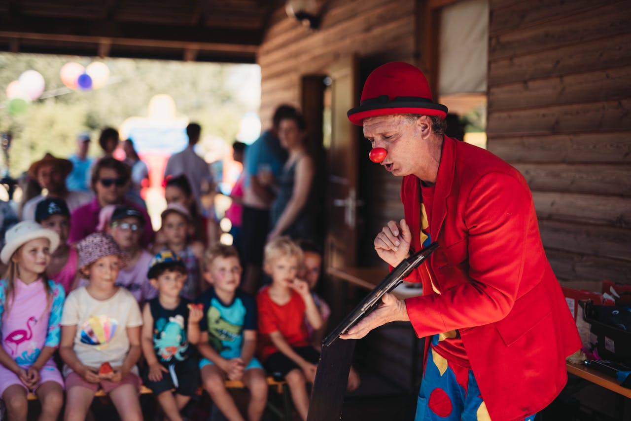 A lively clown performing for a group of children during a sunny outdoor event.