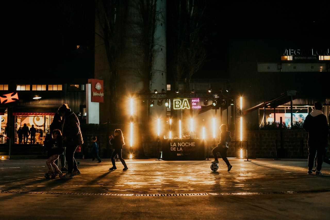 who-we-are Children playing soccer at night in a vibrant urban setting with glowing street lights.